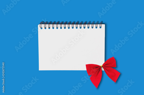 One paper notebook with spiral wire and red festive textile tied bow in center on blue table.  Top view. Holidays concept © OlekStock