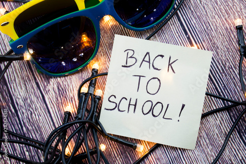 Scattered Lighted Tiny LED Stringlight on Wooden Surface. Two Colorful Sunglasses with Light Reflecting. Handwritten Message Reminding Back To Schooltime photo