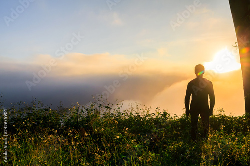 Silhouette of man standing on top mountain looks into the distance at morning misty landscape