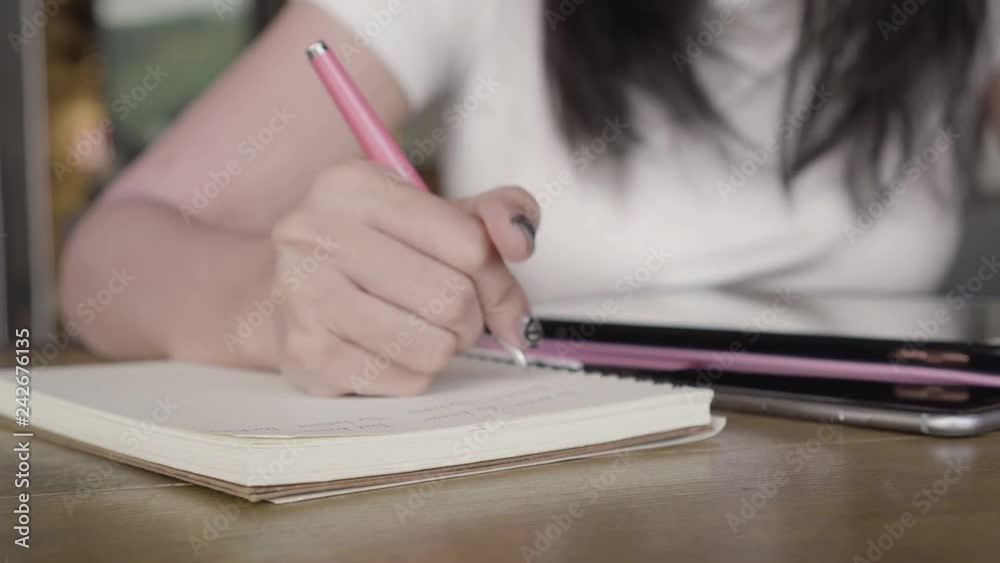 Close up woman hand writing her idea and content on notebook with pen on wooden table with tablet, smartphone in cafe. Close up woman hand writing her idea and content on notebook with pen on wooden table with tablet, smartphone in cafe.