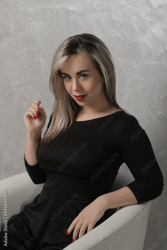 Beautiful girl with red lips and in a black dress sitting in a chair against the background of a gray concrete wall. emotion. different poses Beautiful girl with red lips and in a black dress sitting in a chair against the background of a gray concrete wall. emotion. different poses