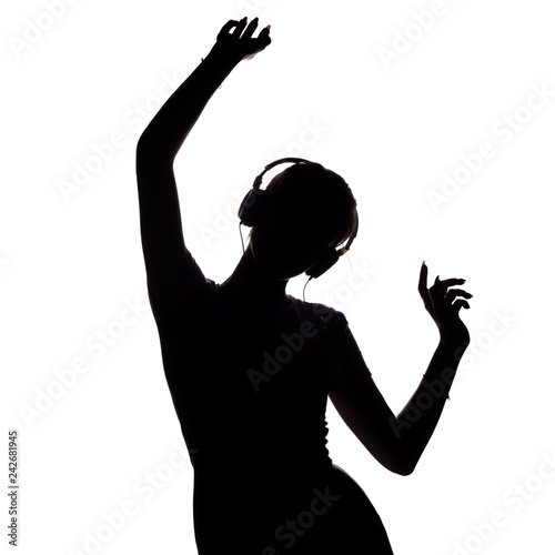silhouette of a happy girl listening to music in headphones, figure of young woman with hands up relaxing on a white isolated background and dancing to the music