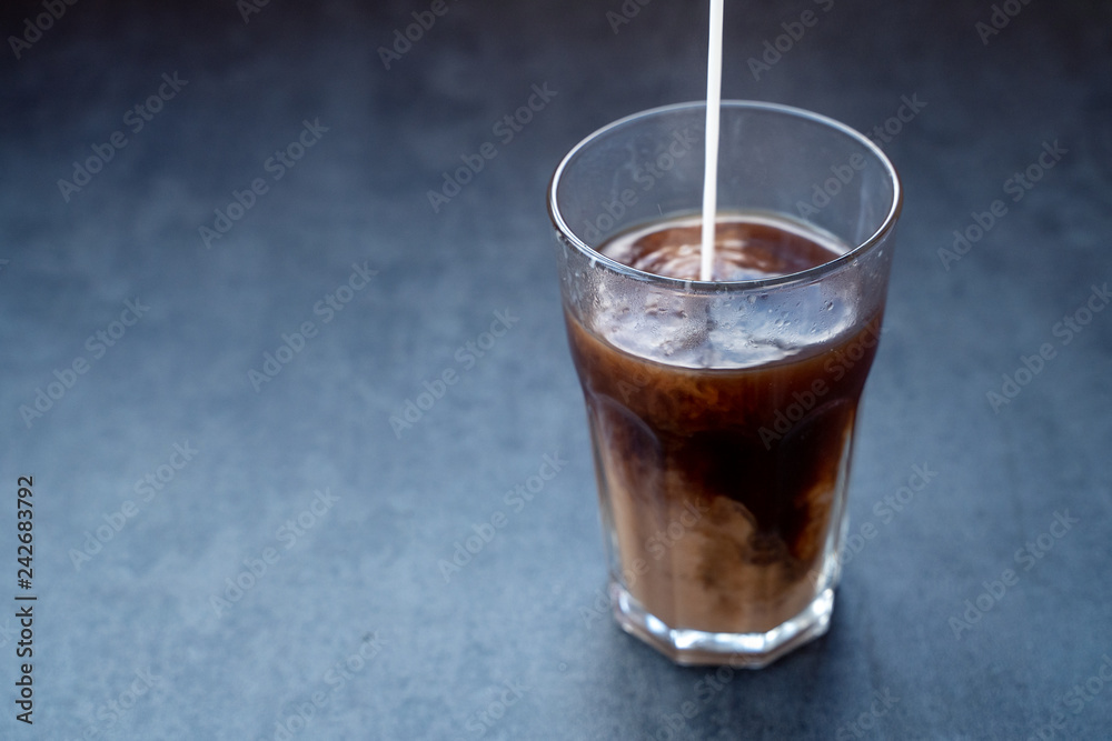 Pouring milk into coffee latte in the glass on a dark gray stone table, copy space. Pouring milk into coffee latte in the glass on a dark gray stone table, copy space.