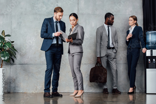 focused multiethnic businesspeople in formal wear talking in waiting hall