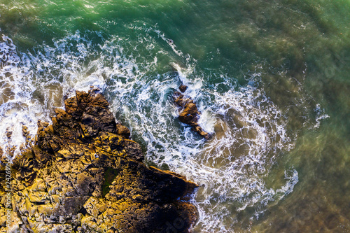 Aerial overhead view of beautiful breaking ocean waves against a rugged rocks