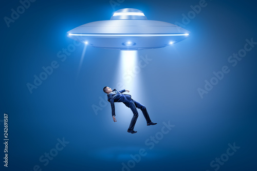 A businessman pulled toward an open hatch of a UFO by some invisible force. © gearstd