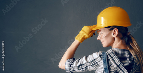 a strong-willed woman in a construction helmet, mittens, goggles and overalls is engaged in repair and construction work at home. concept of a strong and independent woman