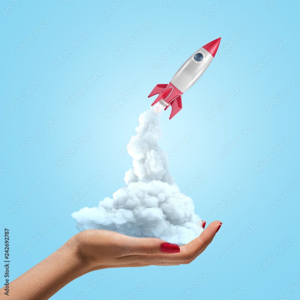 Silver red space rocket launching from female hand on blue background Silver red space rocket launching from female hand on blue background