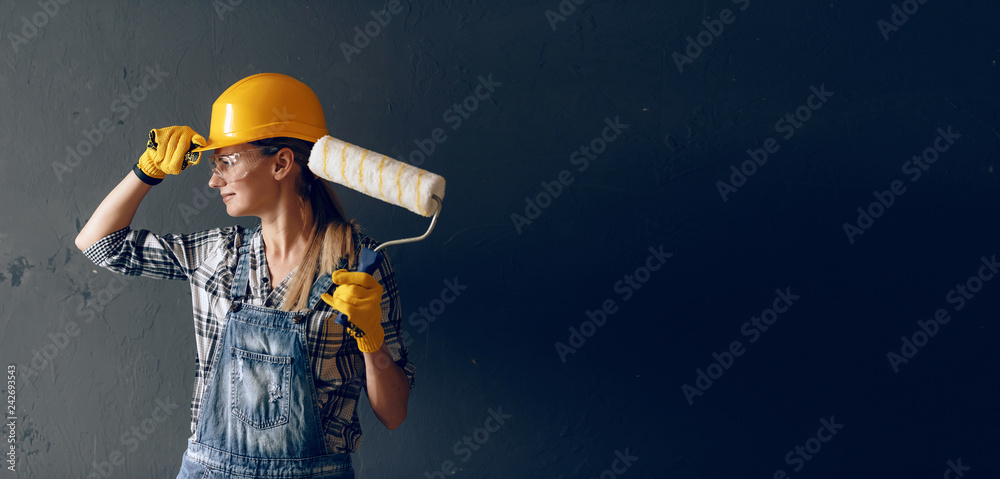 a strong-willed woman in a construction helmet, mittens, goggles and overalls is engaged in repair and construction work at home. concept of a strong and independent woman