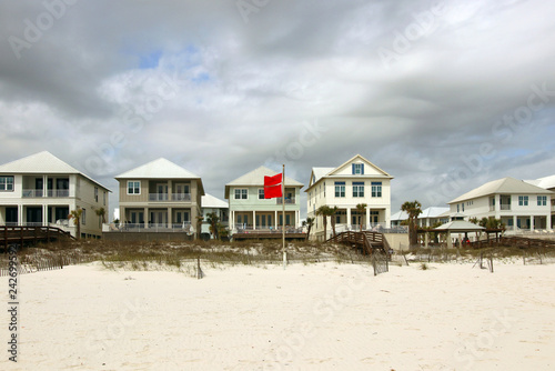 Alabama Gulf of Mexico beach life. Cloudy sky over the oceanfront houses for vacation rental and extremely dangerous warning sing with two red flags in a foreground. 