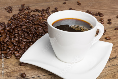 Eine Tasse mit frisch gebrühtem Kaffee und Kaffeebohnen auf einer Holzoberfläche