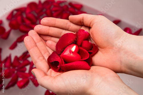 Valentines day surprise, close up woman holding red rose petals and hear candle in hands