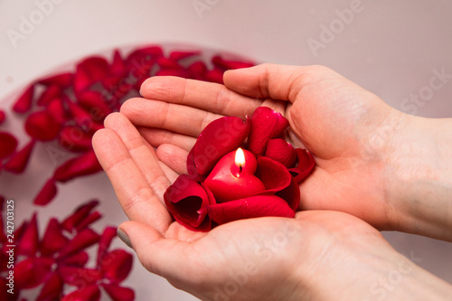 Valentines day surprise, close up woman holding red rose petals and hear candle in hands