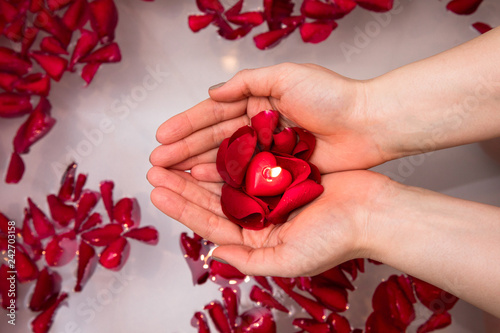 Valentines day surprise, close up woman holding red rose petals and hear candle in hands