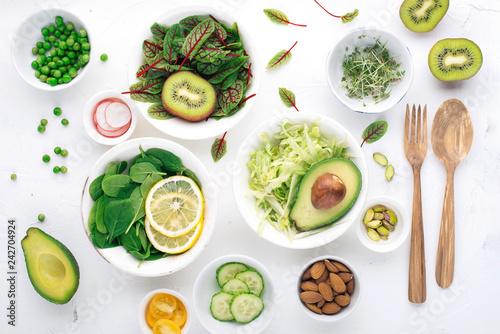 Green ingredients for spring detox salads: spinach, sorrel with red veins, cucumbers, radishes, iceberg lettuce, green peas, avocados, lemon, microgreen, yellow tomatoes on a white background with