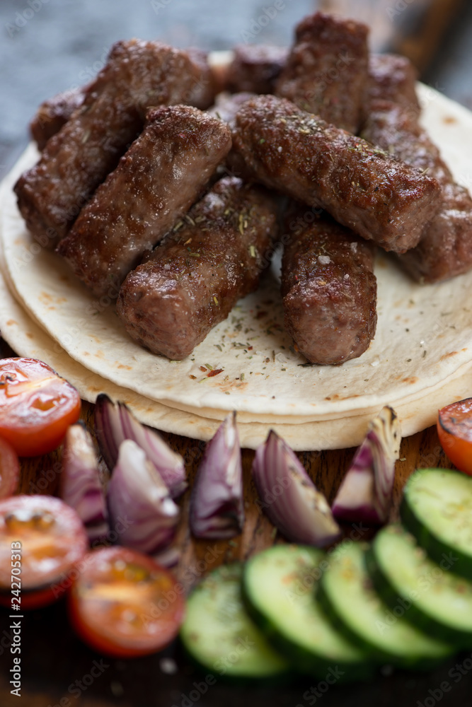 Barbecued balkan cevapi or skinless beef sausages on tortilla flatbread with vegetables, closeup Barbecued balkan cevapi or skinless beef sausages on tortilla flatbread with vegetables, closeup
