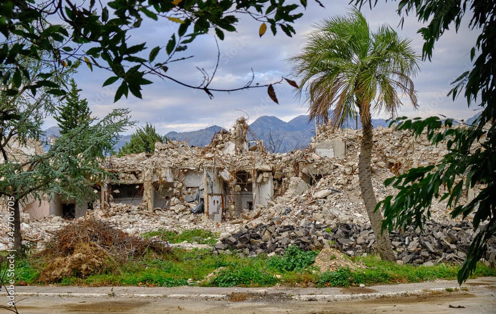 Ruins of a demolished buildings with rubble remaining.  Location is surrounded by mountain and palm trees.  
