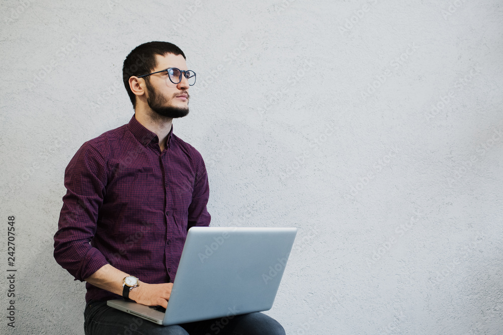 Young pensive bearded guy using laptop, wearing glasses on background of white. Young pensive bearded guy using laptop, wearing glasses on background of white.