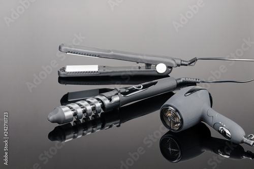 Grey hair iron and grey dryer on the grey mirror background