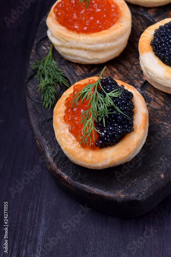 Red and black caviar in tartlets on a wooden board
