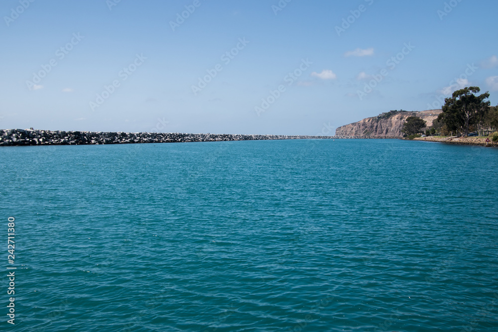 Beautiful large body of calm blue green water with a very long rock jetty on the side and a large cliff in the background.