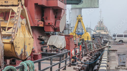 Panorama: Close-up view of cargo port in fog. Tug, floating crane, dry cargo ship, barge and other infrastructure of the port.