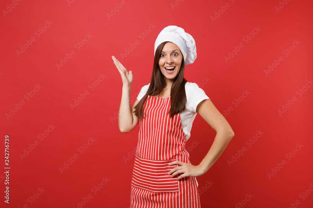 Housewife female chef cook or baker in striped apron, white t-shirt, toque chefs hat isolated on red wall background. Beautiful marvelous housekeeper woman raised hand up. Mock up copy space concept. Housewife female chef cook or baker in striped apron, white t-shirt, toque chefs hat isolated on red wall background. Beautiful marvelous housekeeper woman raised hand up. Mock up copy space concept.