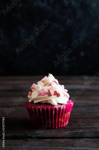 celebratory cupcake for Valentines day and happy birthday on wooden black background with hearts. Give love on a holiday