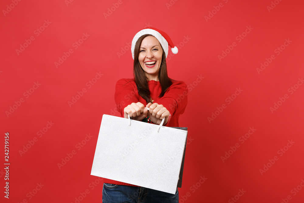 Smiling young Santa girl in Christmas hat holding packages bags with purchases after shopping isolated on red background. Happy New Year 2019 celebration holiday party concept. Mock up copy space. Smiling young Santa girl in Christmas hat holding packages bags with purchases after shopping isolated on red background. Happy New Year 2019 celebration holiday party concept. Mock up copy space.