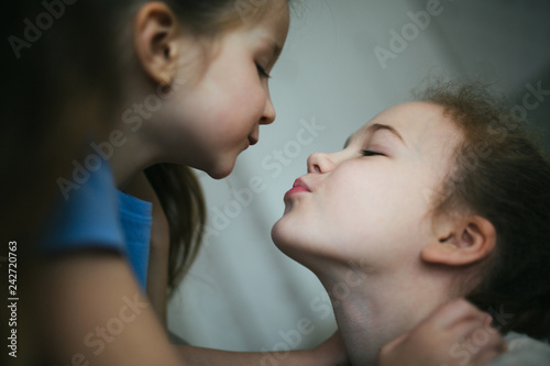 Affectionate girl kissing her happy sister or friend in the living room at home with a homey background