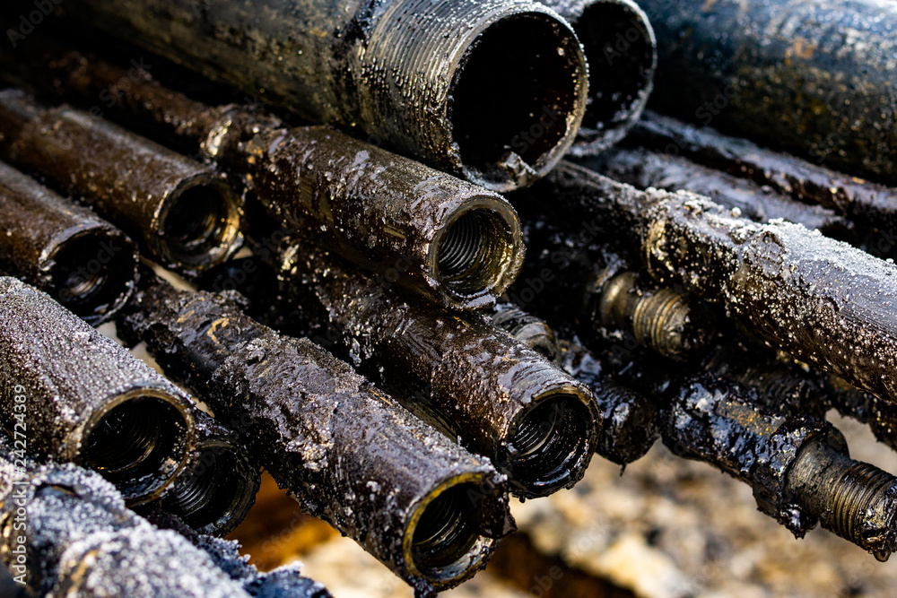 Oil Drill pipe. Rusty drill pipes were drilled in the well section. Downhole drilling rig. Laying the pipe on the deck. View of the shell of drill pipes laid in courtyard of the oil and gas warehouse. Oil Drill pipe. Rusty drill pipes were drilled in the well section. Downhole drilling rig. Laying the pipe on the deck. View of the shell of drill pipes laid in courtyard of the oil and gas warehouse.