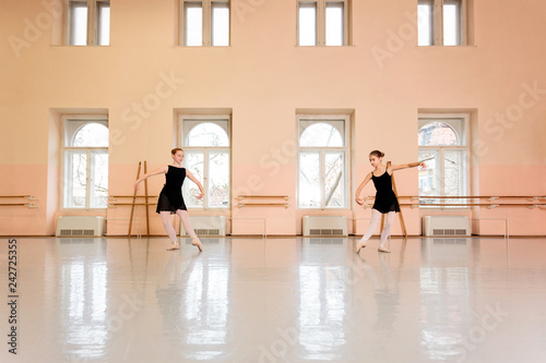 Two teenage girls practicing classical ballet in a large dancing studio. Wide angle view
