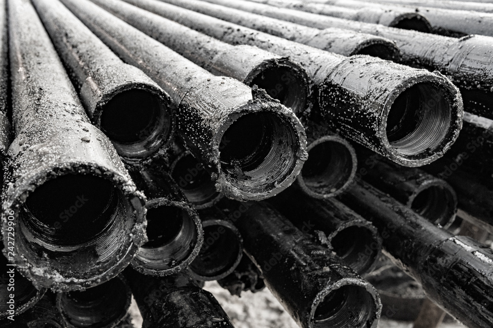 Oil Drill pipe. Rusty drill pipes were drilled in the well section. View of the shell of drill pipes laid in courtyard of the oil and gas warehouse. Black and white photo Oil Drill pipe. Rusty drill pipes were drilled in the well section. View of the shell of drill pipes laid in courtyard of the oil and gas warehouse. Black and white photo