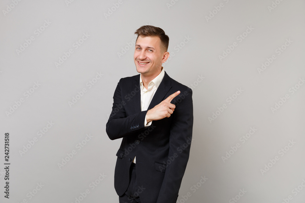 Portrait of attractive young business man in classic black suit shirt pointing index finger aside isolated on grey background in studio. Achievement career wealth business concept. Mock up copy space. Portrait of attractive young business man in classic black suit shirt pointing index finger aside isolated on grey background in studio. Achievement career wealth business concept. Mock up copy space.