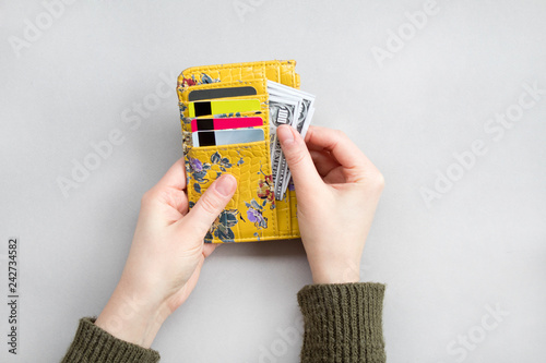 Female hand holding wallet with dollar and bank cards on the grey background.