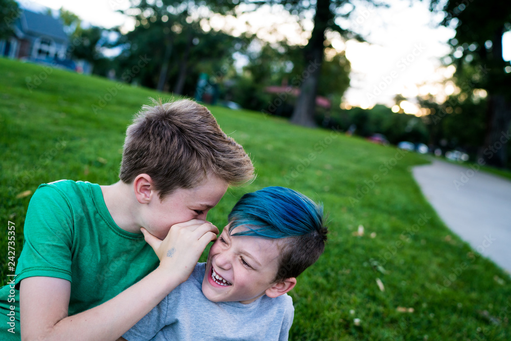 Boy whispering in ear of smiling brother outdoors Boy whispering in ear of smiling brother outdoors