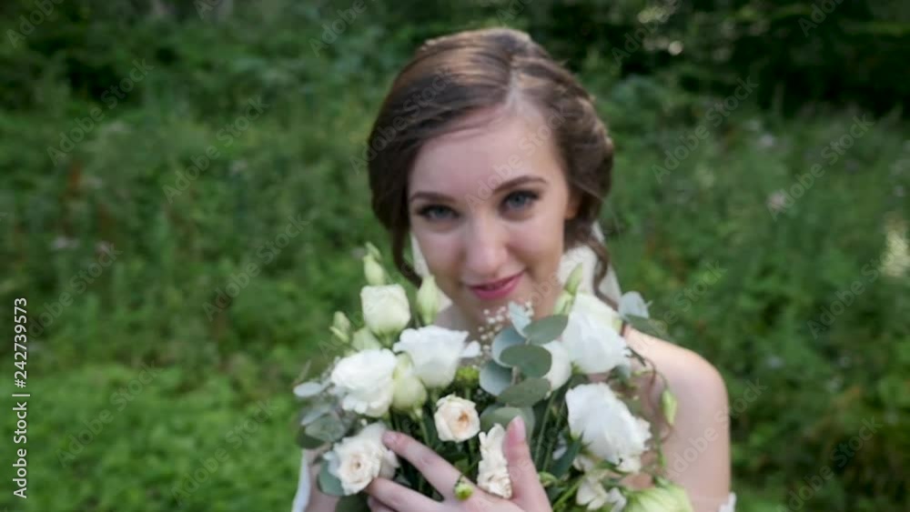 beautiful young bride in wedding dress look at camera and play with flowers in hands in a sunny park. beautiful young bride in wedding dress look at camera and play with flowers in hands in a sunny park.