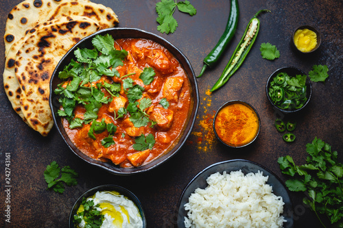 Tableau sur toile Traditional Indian dish Chicken tikka masala with spicy curry meat in bowl, basmati rice, bread naan, yoghurt raita sauce on rustic dark background, top view, close up