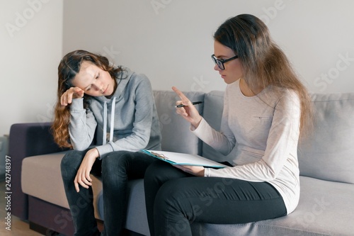 Young woman professional psychologist talking with teenager girl 14, 15 years old sitting in office on sofa. Mental health of child in adolescence