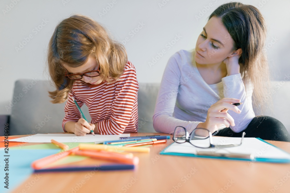 Young female teacher giving private lesson to child, little girl sitting at her desk writing in notebook Young female teacher giving private lesson to child, little girl sitting at her desk writing in notebook