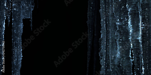 Winter night background. Glittering icicles isolated on black background, blue tones, panoramic view