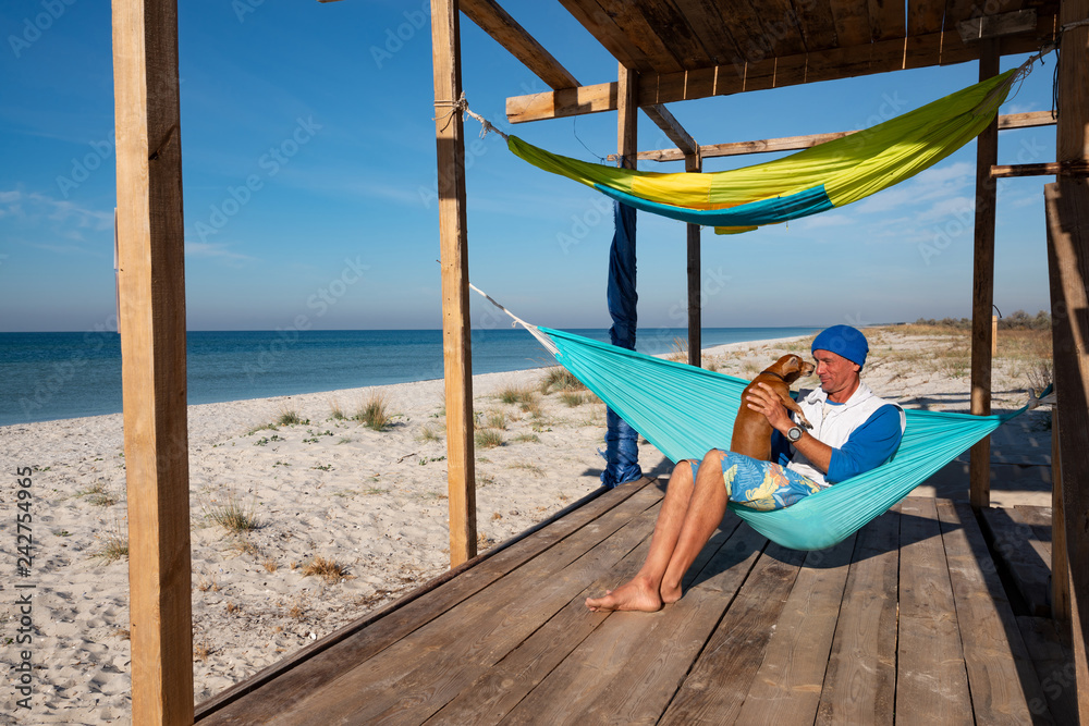 Joyful traveler with funny dog relaxing in a hammock