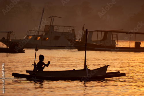 Fisherman Paddling a Small Outrigger in the Village of Pemuteran, Bali, Indonesia. At dawn a fisherman hopes the reef will provide a catch of mackerel to feed his family and provide a small income.