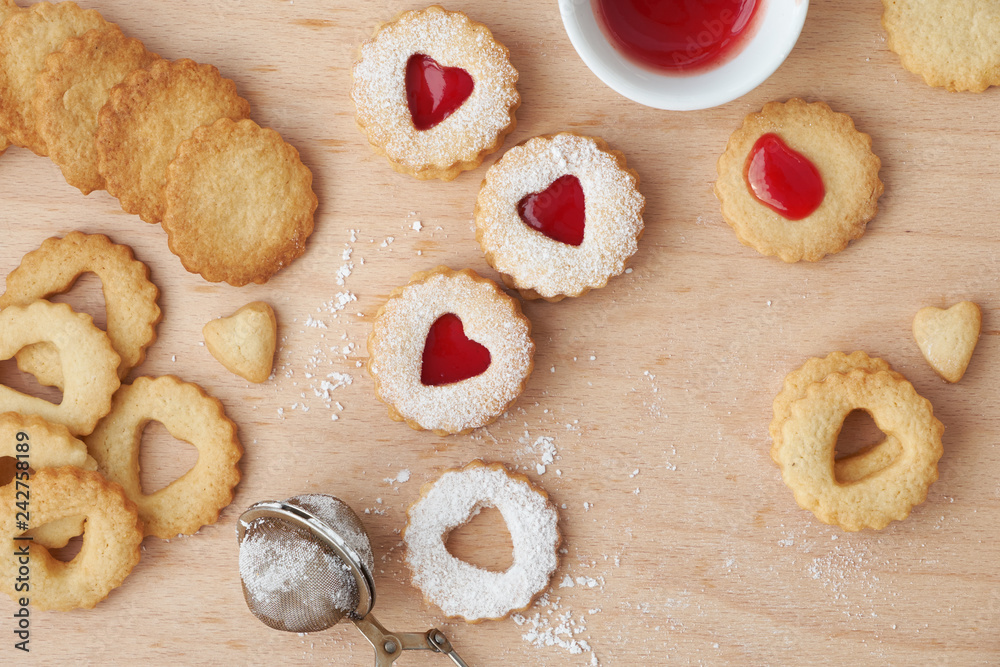 Top view of traditional Linzer cookies filled with strawberry jam on wooden board with heart-shaped openings