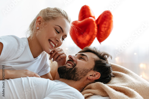Love. Valentine's day. . Emotions. Young couple are looking at each other and laughing while lying together on the bed