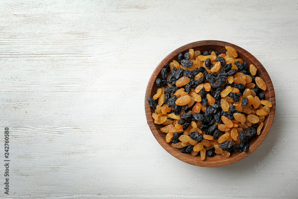 Bowl of raisins on wooden background, top view with space for text. Dried fruit as healthy snack