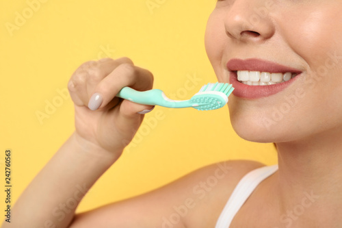 Beautiful woman brushing teeth on color background  closeup