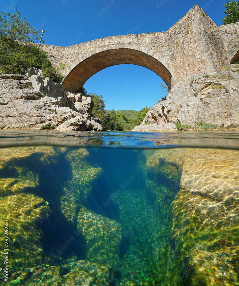 River with an old stone bridge and eroded rocks underwater, split view half above and below water surface, Sant Llorenc de la Muga, Catalonia, Spain