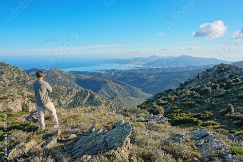 Spain landscape a man standing looking at view from the Albera mountain range with the Mediterranean sea and the Cap de Creus in background, Pyrenees, Catalonia, Alt Emporda