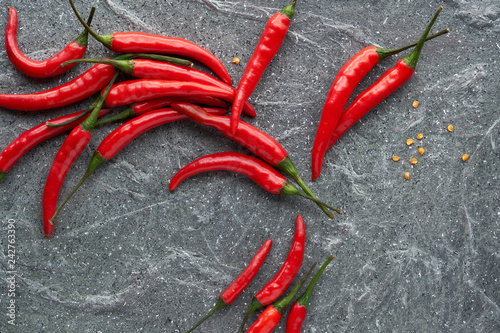 Close-up on red hot chili peppers, fresh and dry, on dark stone, top view